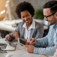 A man and two women at a table using a laptop and tablet
