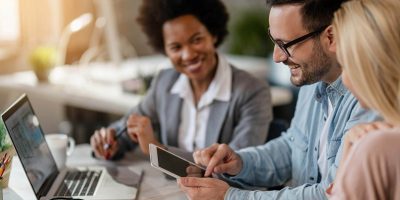 A man and two women at a table using a laptop and tablet