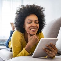A woman laying on a sofa and using a tablet