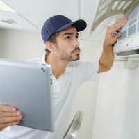 A man on a ladder fixing an HVAC unit