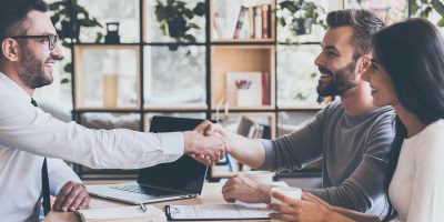 A young couple shaking hands with a man in business attire sitting at a desk