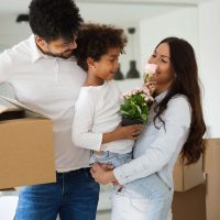 A family smelling a bouquet of flowers, surrounded by moving boxes